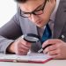 Businessman with magnifying glass studying agreement Businessman with magnifying glass studying agreement